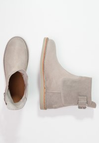 Grå mocka anklar stövlar med rund tå, platt klack, sidobanddetalj och beige gummisula. Slät textur och ren design.