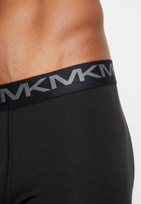 Mustat boxerit venyvää kangasta, joissa on leveä musta vyötärönauha, jossa on harmaata "MK"-kirjoitusta, ja ne tarjoavat sileän pinnan.
