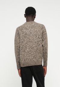 Textured brown knit sweater with a crew neckline, featuring a subtle speckled pattern and long sleeves, worn with black pants.