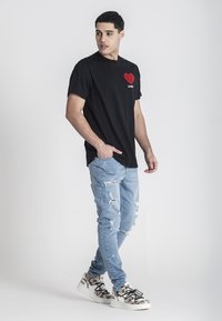 Černé bavlněné tričko s červeným srdcovým grafikou na hrudi, kombinované se světle modrými desgérovými džíny a vzorovanými teniskami.
