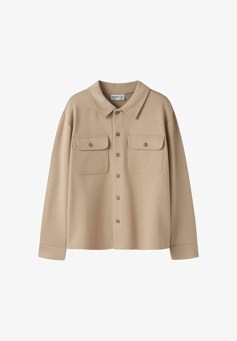 Veste-chemise beige à manches longues avec col, boutons sur le devant et deux poches poitrine boutonnées sur fond blanc.