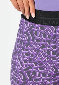 Sport leggings med en sort elastisk talje. Stoffet har et lilla geometrisk mønster på en grå baggrund. Struktureret overflade.
