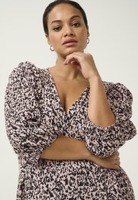 Vestido romántico con estampado de animal en negro y rosa, escote en V profundo, mangas abullonadas y tejido texturizado que realza el interés visual.