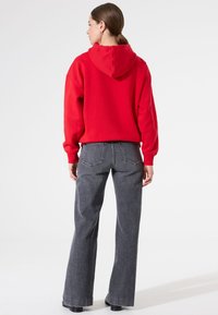 Sudadera roja con capucha de corte relajado, combinada con jeans de pierna ancha grises que cuentan con bolsillos traseros y una textura ligeramente desteñida.