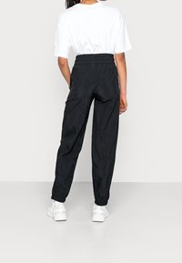 Zwarte, lichte, elastische broek met een losse pasvorm en gathered cuffs, gecombineerd met een eenvoudige witte t-shirt en witte sneakers.