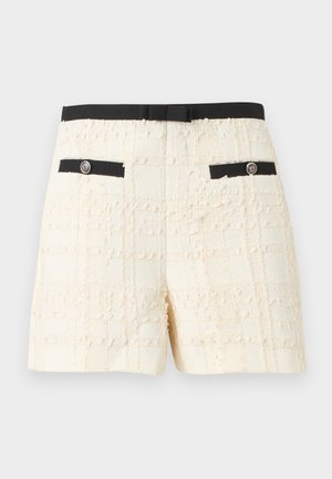 Kremfargede shorts med svart midjebånd og dekorative lommer med svarte kanter, på ensfarget bakgrunn.