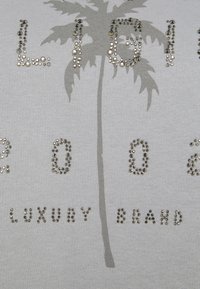 Maglione grigio con grafica di una palma e decorazioni di strass argentati che scrivono "LIG 2002 LUXURY BRAND". Morbida trama a maglia.