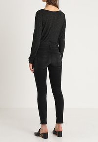 Top negro de manga larga con un corte holgado, combinado con unos jeans skinny negros de cintura alta, textura suave y bolsillos traseros. Mules negros de tacón cuadrado.