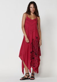 Rotes ärmelloses Kleid mit asymmetrischem Saum, mit schwarzem Blumenmuster und dekorativen Perlenakzenten im Oberteil. Weicher, leichter Stoff.