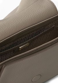 Borsa a tracolla in pelle taupe chiaro con superficie testurizzata; presenta un interno spazioso con fodera decorata e una targhetta metallica con il marchio.