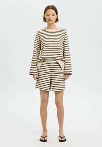 Béžový a černý pruhovaný set pohodlného oblečení obsahující top s dlouhým rukávem a širokými rukávy, spolu se shodnými šortkami s elastickým pasem.