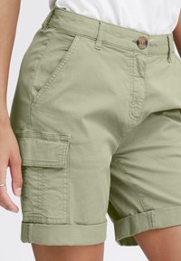Világoszöld szövet cargo shorts, pamut keverékből készült. Jellemzői közé tartozik a feltekert szár, első zsebek és egy oldalsó zsebtartó zseb.