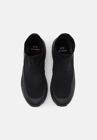 Svarta slipskor med överdel av stickad textil och slät gummisula. Har en låg ankel-design och diskret logotypdetalj på innersulan.