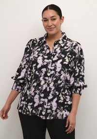Schwarze Bluse mit einem bunten abstrakten Muster in Rosa- und Grüntönen, mit einer Knopfleiste vorne und Rüschendetails an den Manschetten.
