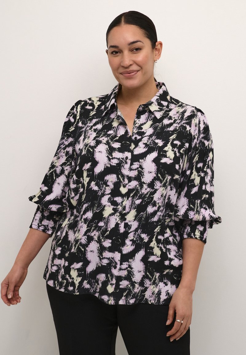 Schwarze Bluse mit einem bunten abstrakten Muster in Rosa- und Grüntönen, mit einer Knopfleiste vorne und Rüschendetails an den Manschetten.