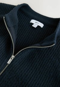 Pulover tricotat bleumarin cu dungi, guler înalt și fermoar argintiu. Eticheta indică "NEXT," mărimea M. Material texturat cu detaliu de fermoar în contrast.