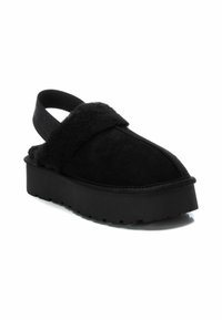 Sandali platform neri realizzati in morbido suede con una parte superiore pelosa, una larga fascia sul piede e un design con cinturino sul retro per una facile indossabilità.