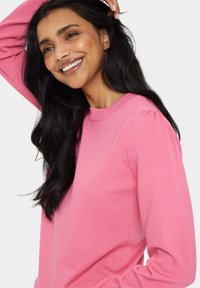 Ilgi piedurkņu, apaļas kakla džemperis dzīvīgā rozā krāsā, ar ribotām apkakles un piedurkņu detaļām, kā arī mīkstu, gludu tekstūru.