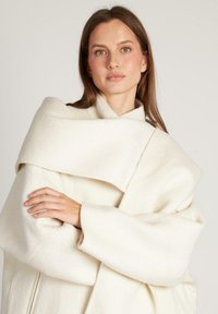 Cappotto bianco in lana con design drappeggiato, ampio colletto e maniche oversize, caratterizzato da una trama liscia e dettagli di cucitura minimi.