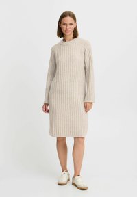 Strickkleid mit Rippenmuster in hellem Beige, Rundhalsausschnitt und langen Ärmeln, kombiniert mit weißen Sneakers mit beiger Sohle.