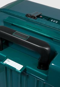 Turchese harde koffer met een gestructureerd oppervlak, zwart handvat, dubbele rits, ingebouwd slot en een houder voor een ID-label aan de voorkant.