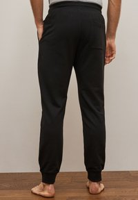 Sorte bomuldsjoggingbukser med en afslappet pasform, elastisk talje og ribbede manchetter. Baglomme med detaljer synlig. Enkel design, blød tekstur.