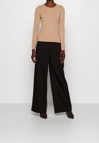 Beige Fitted Pullover mit langen Ärmeln, kombiniert mit weit geschnittenen schwarzen Hosen, akzentuiert durch dunkle Schuhe. Weiche Textur beider Teile.