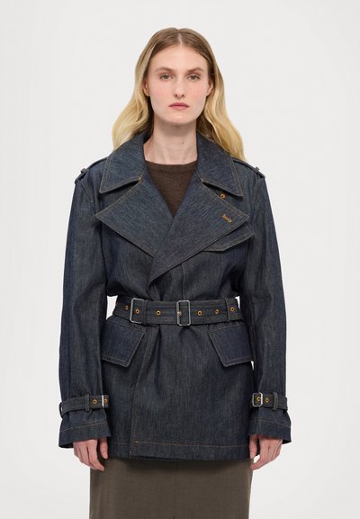 Manteau en denim avec large col, taille ceinturée et poignets boutonnés. Tissu bleu foncé avec couture orange contrastante et deux poches avant.