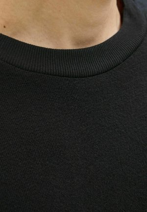 Sweatshirt noir avec un col rond côtelé et un matériau texturé. Vue en gros plan mettant en évidence le motif tissé du tissu et sa douceur.