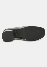 Chaussure à talon haut en cuir noir avec un bout arrondi et une semelle extérieure en caoutchouc texturé. L'intérieur présente une doublure marron avec une marque.
