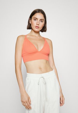 Top desportivo coral com um design em forma de V, feito de material canelado. Alças ajustáveis e um corte cropped, combinado com calças de cordão de cor clara.