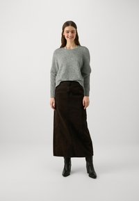 Grå tröja med långa ärmar, kombinerad med en brun maxikjol. Outfitten har en avslappnad passform och enkel design. Bärs med svarta ankelstövlar.