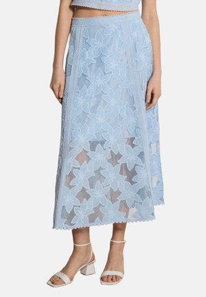 Gonna midi in pizzo floreale azzurro chiaro indossata con sandali bianchi con tacco, che mostra un sovrapposizione trasparente con motivi floreali e orlo smerlato.