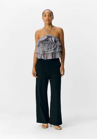 Halsloze top met gelaagd gerimpeld stof in grijs en lavendel, gecombineerd met zwarte wijde broek en beige hoge sandalen.