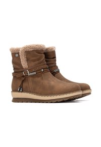 Botas de tobillo marrones con forro de pelaje sintético, hebillas decorativas y acentos metálicos. Tienen una suela gruesa y un material superior texturizado.