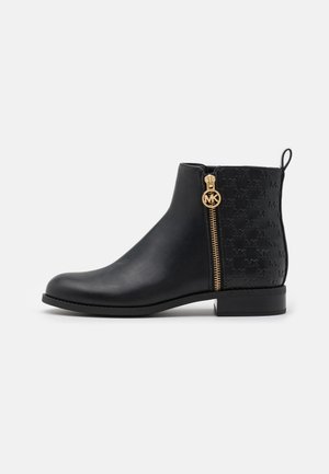 Bottine noire avec motif embossé à l'arrière, fermeture éclair dorée et tirette circulaire avec logo MK, et talon empilé bas.