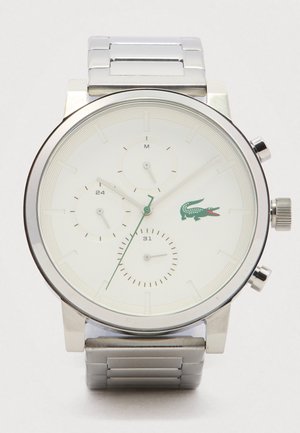Srebrni metalni ručni sat s bijelim brojčanikom, tri podbroja i zelenim krokodilskim logotipom s desne strane, sačinjeno od narukvice od nehrđajućeg čelika.