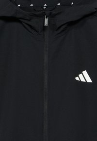 Μαύρο μπουφάν με κουκούλα από λείο ύφασμα, με κεντρικό φερμουάρ και λευκό λογότυπο στο κάτω δεξί  μέρος. Διακριτικό μοτίβο στολισμού κατά μήκος της κουκούλας.