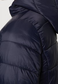 Närbild av en marinblå vadderad vinterjacka med horisontell kviltad sömnad och hög krage.