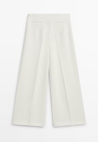 Pantalon à jambes larges de couleur crème clair, avec une texture de tissu lisse, des plis à l'avant et deux poches arri ère.