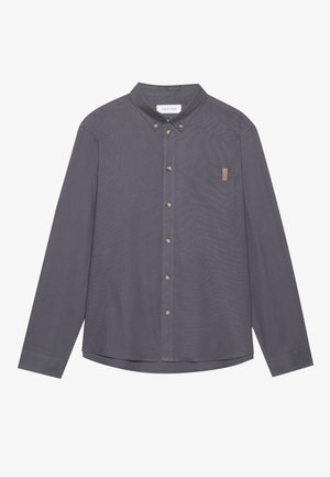 Chemise grise à manches longues avec un bouton, une poche, un col et une texture subtile. Dotée de boutons en métal et d'une petite étiquette en cuir sur la poche.