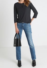 Svartvitt prickigt långärmad topp, blå raka jeans, svart strukturerad handväska och svarta spetsiga ankelstövlar.