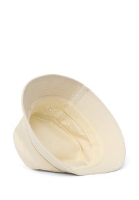 Cappello a secchiello in cotone color beige chiaro con una larga visiera curvata. L'interno è caratterizzato da cuciture e fori di ventilazione, con una texture morbida.