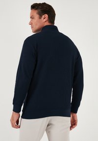 Navy blue pullover with a high collar, ribbed texture, and long sleeves. Features a relaxed fit and solid color without additional patterns.
