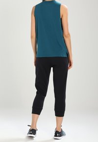 Turkos ärmlös topp, svarta korta sweatpants och svarta träningsskor. Toppen har en rundad halslinning; byxorna har uppvikta nederkanter.