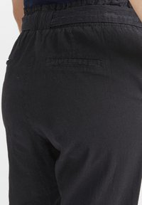 Black trousers with an elastic waistband, featuring a single back pocket and a textured fabric. The design is relaxed-fit with a smooth finish.