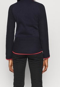 Marineblauwe pullover met lange mouwen, voorzien van een rode rand bij de manchetten en de zoom, gemaakt van een gestructureerde stof met een aansluitende pasvorm.