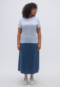 Ανοιχτό μπλε βαμβακερό t-shirt με κοντά μανίκια, συνδυασμένο με μακριά τζιν φούστα. Το μοντέλο φοράει λευκά αθλητικά παπούτσια και στέκεται σε απλό φόντο.