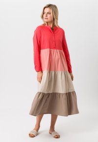 Kleurblok jurk met een koraal bovenstuk met knoopsluiting, overgaand naar een lichtroze, crème en bruine gerimpelde onderkant. Lange mouwen.