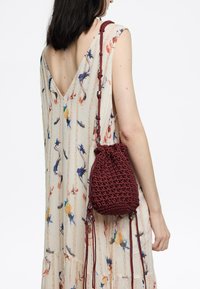 Bolsa de algodón burdeos con cordón de tiro y un acabado texturizado, combinada con un vestido color crema con estampado floral y escote en V.